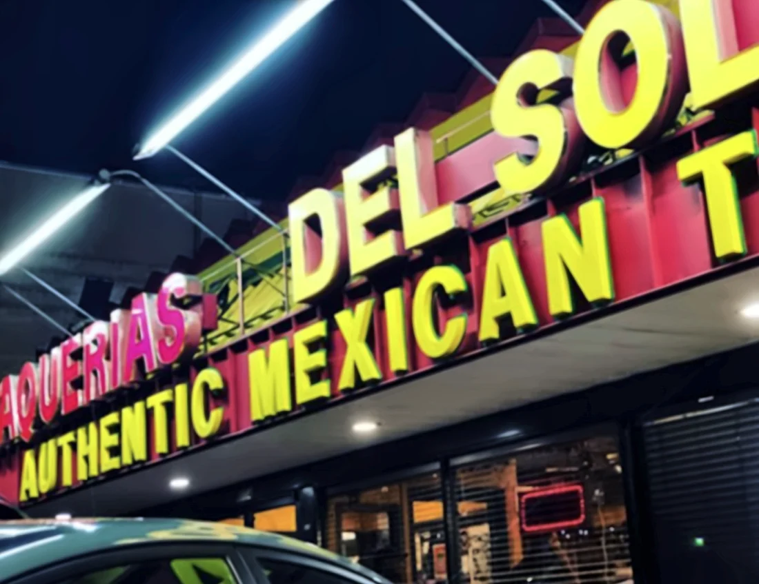 The lit Taquería Del Sol sign at night